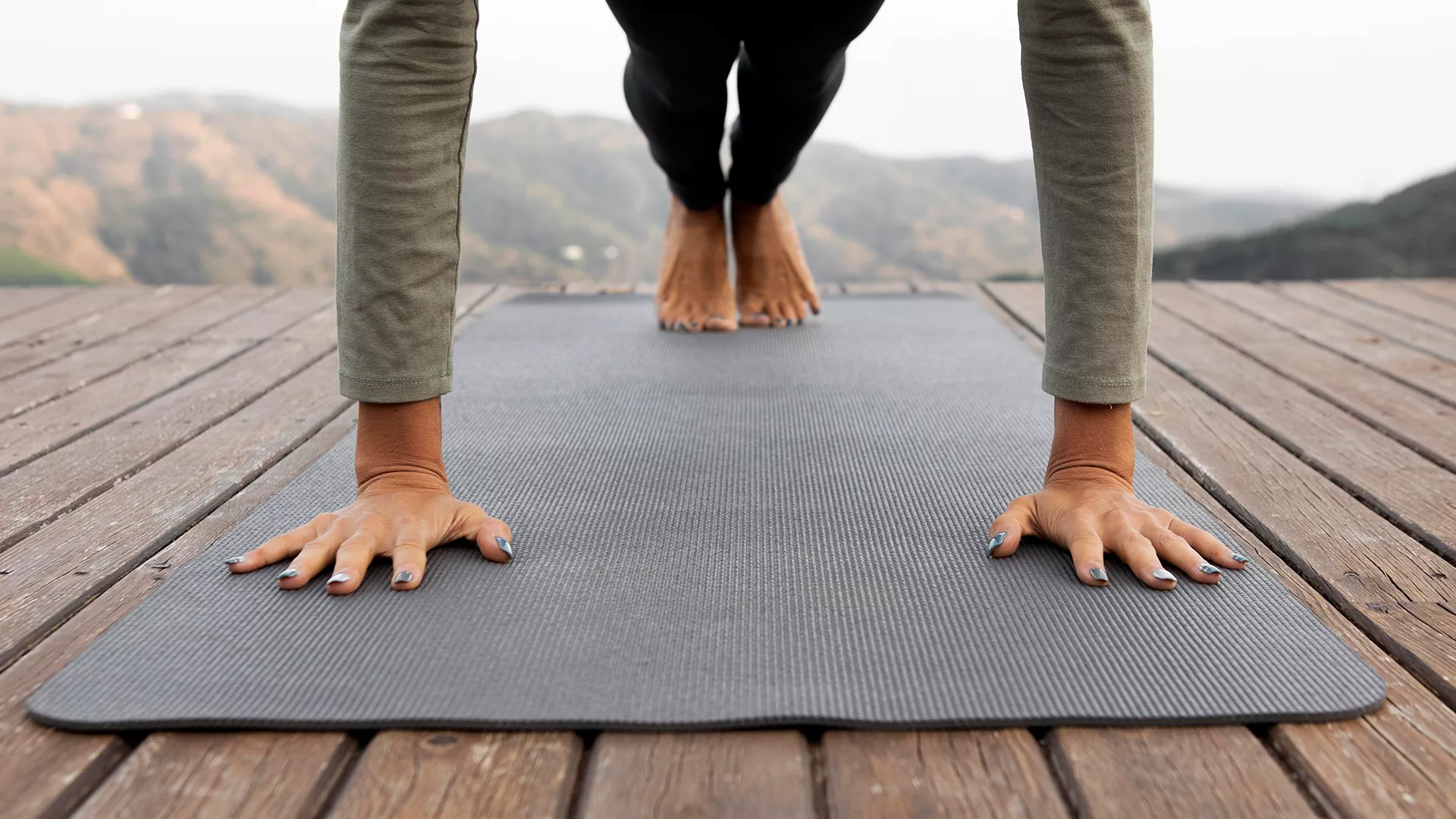 une femme faisant une planche sur un tapis de yoga sur un sol en bois avec un fond montagneu
