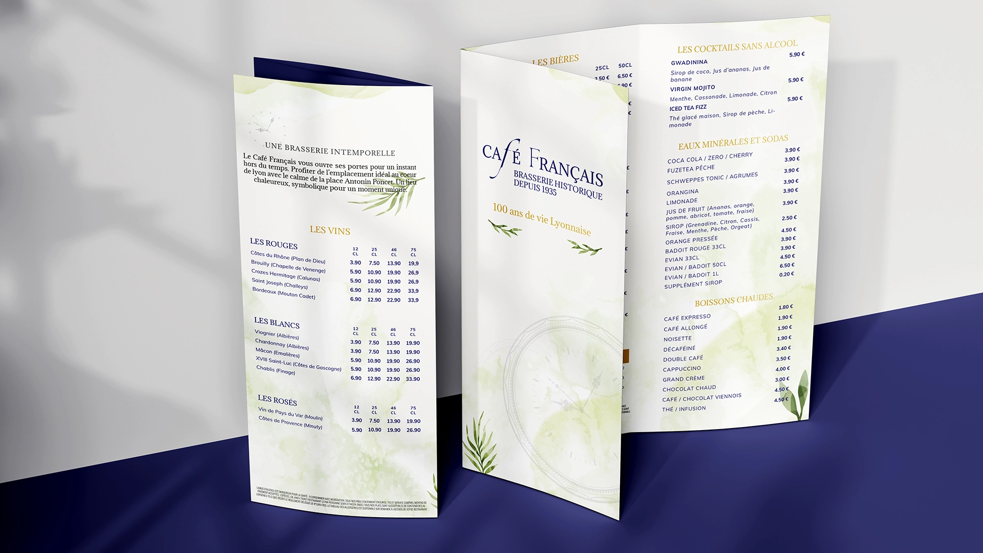 Carte et Menu en tryptique mise en situation, posée sur un fond bleu, et un mur beige avec des ombres